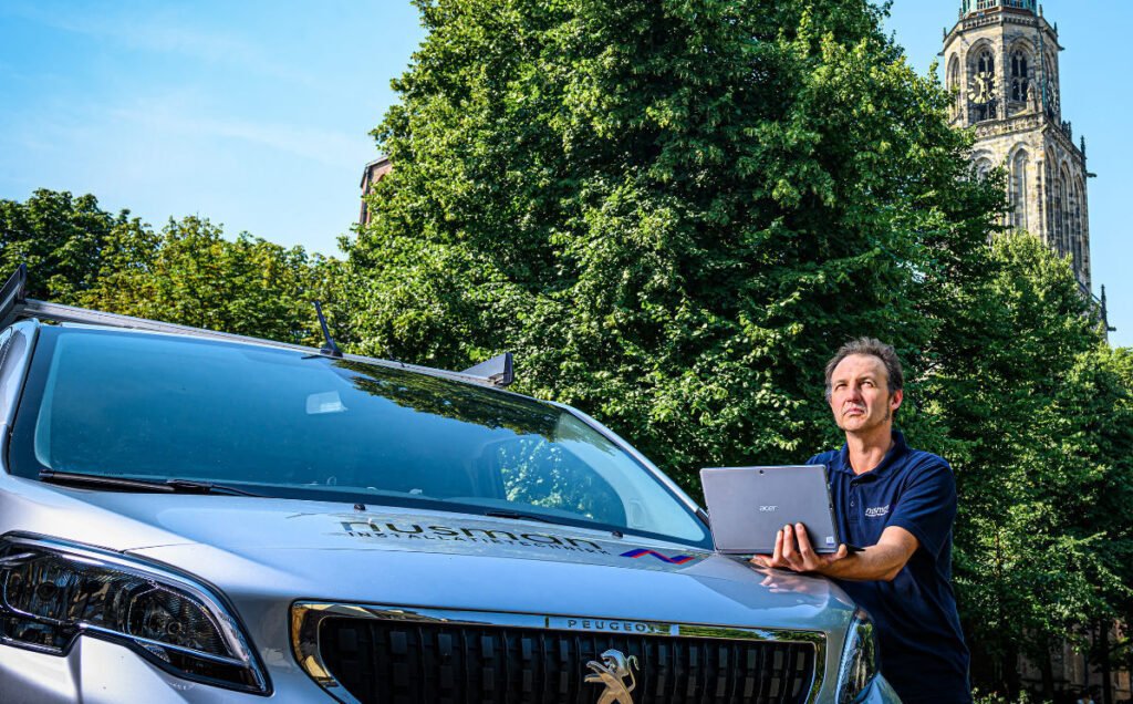 Een man staat naast een bestelwagen en houdt een laptop in haar hand.