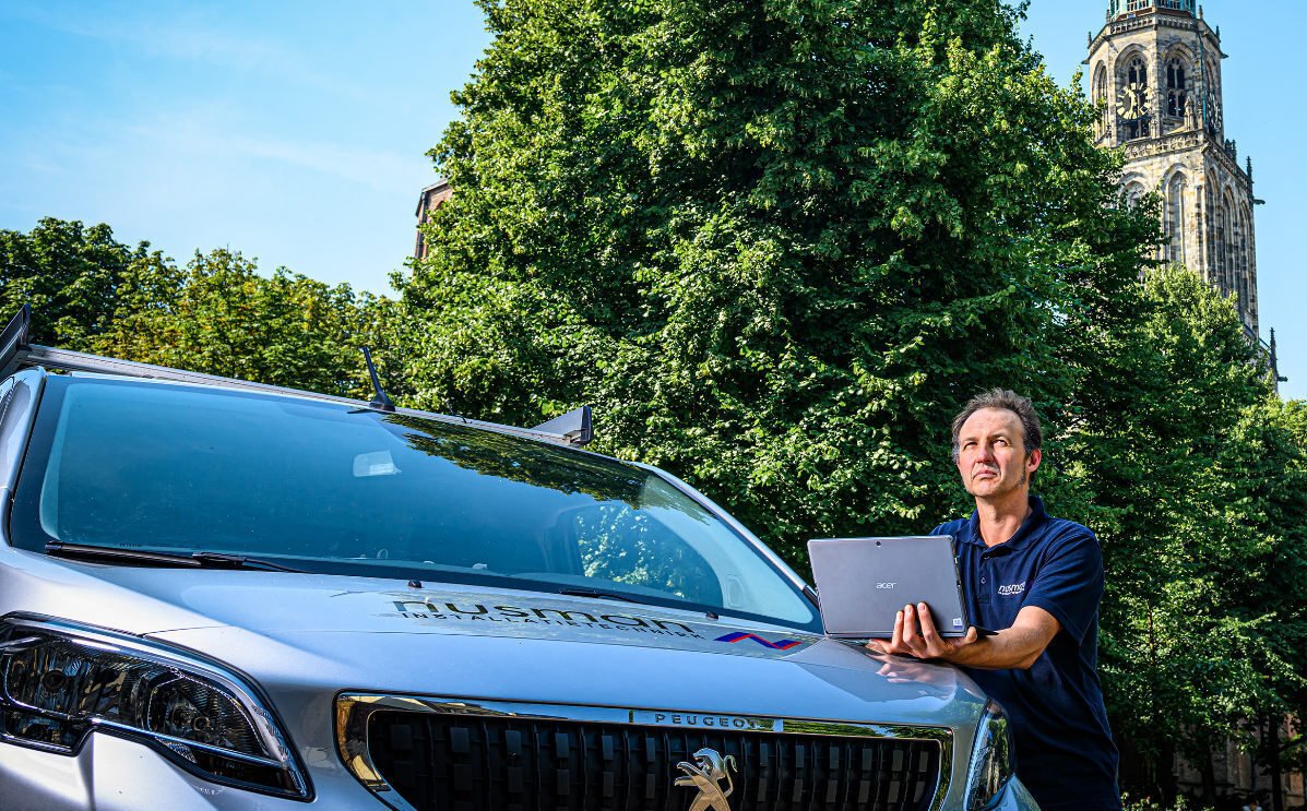 Een man staat naast een bestelwagen en houdt een laptop in haar hand.