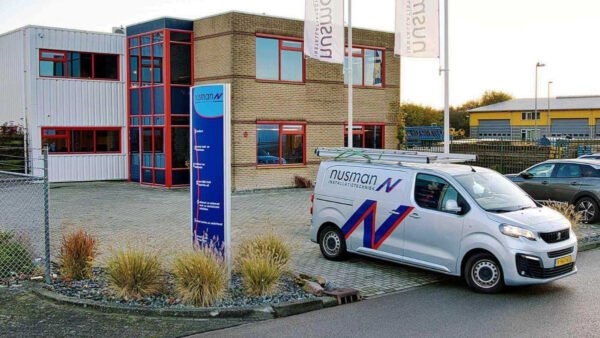 Een bus staat voor een gebouw met een auto reclame dat "Nusman" aangeeft.