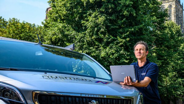 Een man houdt een laptop vast naast een busje.