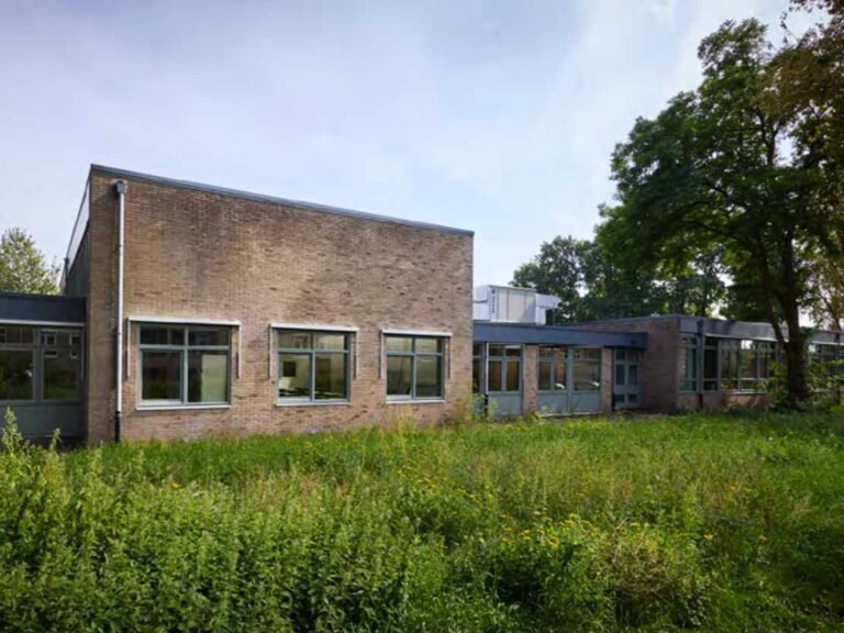 Bakstenen voorgevel van het gerenoveerde schoolgebouw aan de Bessemoerstraat in Groningen met ramen en een groene grasstrook