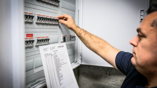 Specialist van Nusman Installatietechniek Groningen die een elektrische installatie controleert met behulp van handleidingen voor camerabeveiliging, brandbeveiliging en inbraakbeveiliging.