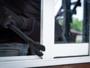 Een inbreker met handschoenen gebruikt een koevoet om een raam open te breken.