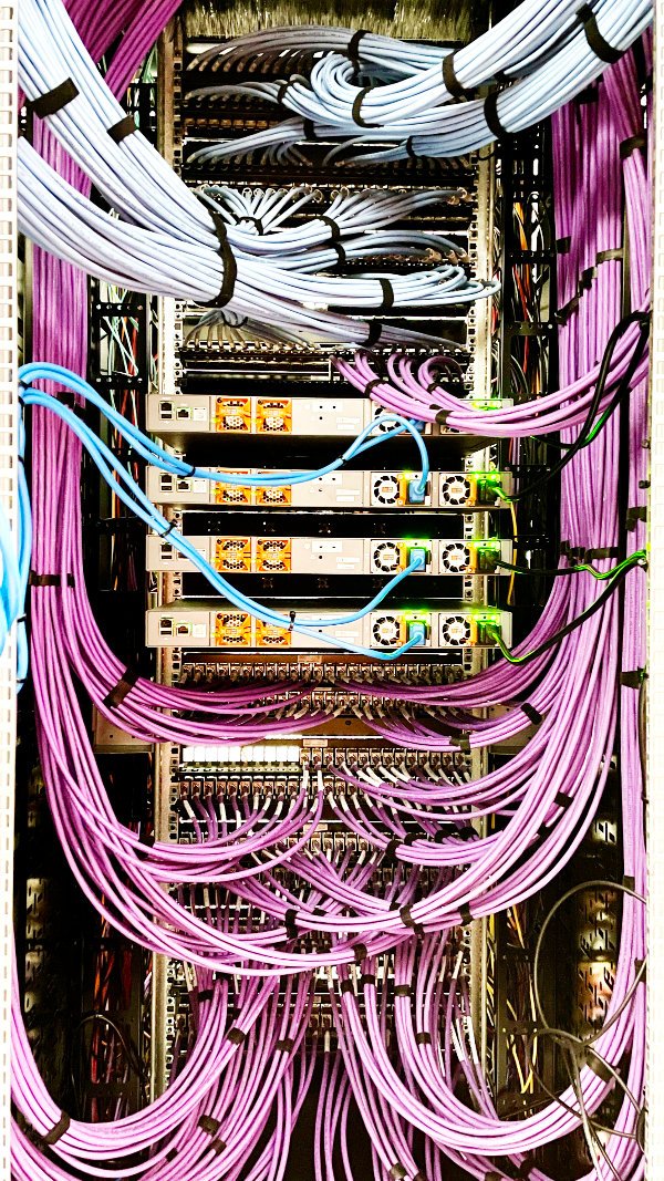 Gestructureerde paarse en witte netwerkkabels gemonteerd in een serverkast door Nusman Installatietechniek bij RTV Noord