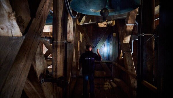Inspecteur van Nusman Installatietechniek voert een veiligheidsinspectie uit in een kerktoren met luidklok.