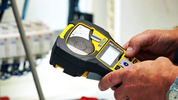 Monteur gebruikt een Brady BMP21-PLUS labelprinter voor het coderen en labelen van een elektrische installatie tijdens een NEN 1010 inspectie.