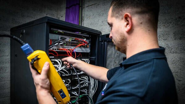 Netwerkspecialist van Nusman Installatietechniek test netwerkkabels in een serverkast met een netwerktester.